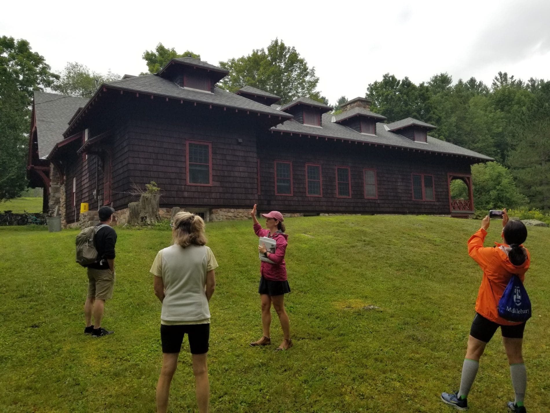 A woman leading a tour group on the lawn of a historic gate lodge.